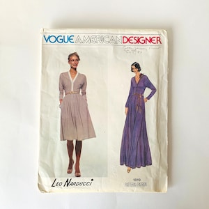 May include: Vogue American Designer sewing pattern #1819 by Leo Narducci for a dress with long sleeves and a V-neck. The pattern shows two models wearing the dress in different lengths, one in a light gray color and the other in a purple color.