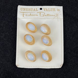 Puede incluir: Seis botones de moda vintage sobre una tarjeta blanca. Cada botón presenta un centro ovalado opalescente rodeado por un marco de metal dorado tejido. La tarjeta dice "UNUSUAL VALUE in Fashion Buttons."