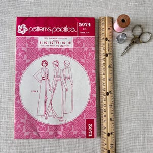 May include: A vintage sewing pattern package from Patterns Pacifica, featuring illustrations of long dresses. The package is pink with the number 3074 and size details. A wooden ruler, scissors, thimble, and thread spool are also visible.