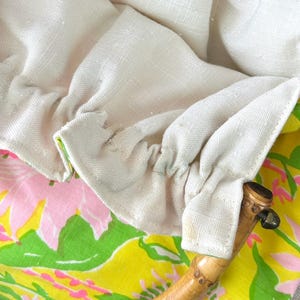 May include: A handbag featuring a bright yellow fabric exterior with a pink and green floral pattern. The bag has a gathered off-white linen lining and a curved, segmented bamboo handle attached to the fabric with stitched fabric loops.