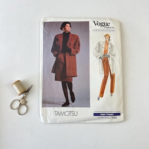 May include: A vintage Vogue Patterns sewing pattern featuring a woman in a rust-colored coat and skirt ensemble. The pattern is labeled "AMERICAN DESIGNER" and includes the text "TAMOTSU" and "EASY/FACILE PATTERN/PATRON 1953". A spool of thread and scissors are in the image.