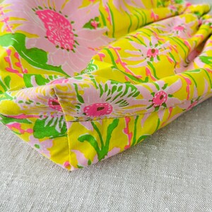 May include: A fabric handbag featuring a vibrant floral pattern with large pink and white flowers, bright green leaves, and a yellow background. The bag includes a curved bamboo handle attached to the top, showcasing a gathered, soft construction.