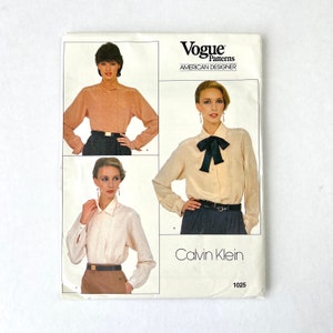 May include: Vogue Patterns American Designer sewing pattern for a blouse by Calvin Klein. The pattern shows three different styles of blouses with long sleeves and a collar. The pattern number is 1025.