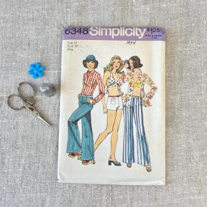 May include: Vintage Simplicity sewing pattern number 6348 for a women's outfit. The pattern is for a size 12, bust 34 inches, and is for misses. The pattern is from 1974 and features three different outfits: a striped shirt with bell bottom pants, a halter top with shorts, and a floral print top with striped pants.