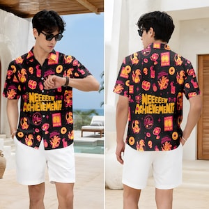 May include: A black short-sleeved button-down shirt featuring a vibrant all-over print of yellow and pink graphics, including skulls, trophies, and donuts, with the bold yellow text "NEEEEEW ACHIEVEMENT!" printed across the center of the chest.