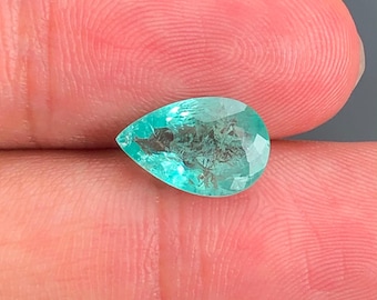 Könnte beinhalten: Ein birnenförmiger, facettierter Edelstein in leuchtendem Türkisgrün mit sichtbaren Einschlüssen. Der Stein hat eine polierte Oberfläche mit zahlreichen dreieckigen Facetten, die das Licht reflektieren und eine durchscheinende Qualität sowie einen hellen, gesättigten Farbton aufweisen.