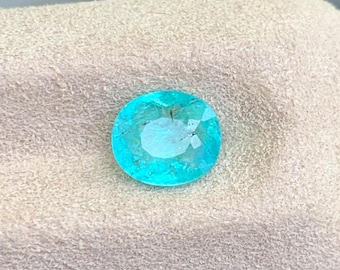 Könnte beinhalten: Ein loser, oval geschliffener Edelstein in einer leuchtenden, durchscheinenden blau-grünen Neonfarbe. Der Stein besitzt eine facettierte Oberfläche, die das Licht reflektiert und die innere Reinheit sowie natürliche Einschlüsse zeigt.