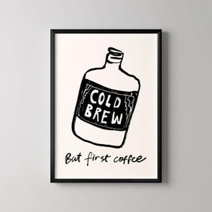 Peut inclure: Impression d'art encadrée en noir et blanc avec une illustration dessinée à la main d'une bouteille de café infusé à froid. La bouteille porte une étiquette avec l'inscription "COLD BREW". En dessous, le texte dit "But first coffee".