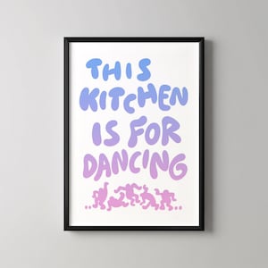 May include: A framed art print with the text "THIS KITCHEN IS FOR DANCING" in blue and purple gradient lettering. Below the text are stylized dancing figures in pink. The black frame surrounds the white background.