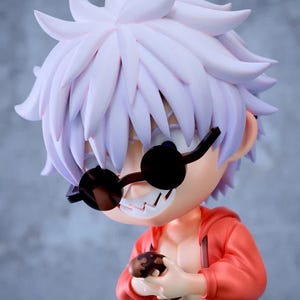 May include: A figurine of a cartoon character with spiky white hair, wearing black sunglasses and a red jacket. The character is holding a small, brown object and has a mischievous grin. The figure has a stylized design.