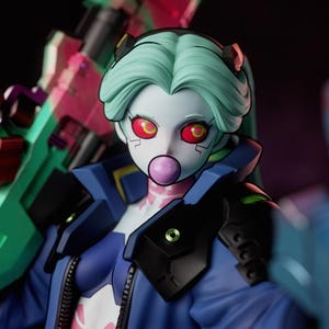 May include: A collectible figurine featuring a character with pale skin, mint green hair, and red eyes, blowing a pink bubble. The figure wears a blue jacket with black armour plating and holds a large green and pink weapon. Text reads PATREON GatsuStudios.