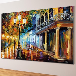 Puede incluir: Pintura al óleo de una calle de la ciudad por la noche, con una farola y edificios. La obra de arte presenta colores vibrantes, incluyendo naranja, amarillo y azul, reflejados en el pavimento mojado. Una persona con un paraguas camina por la calle.
