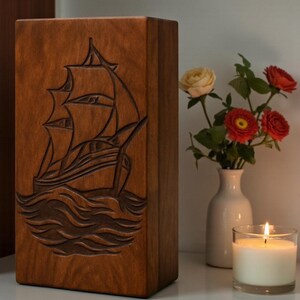 Handcrafted wooden funeral urn box with a nautical ship engraving on the lid. The elegant wood finish and professional carving make it a timeless tribute for a loved one’s ashes. Designed for home display, memorial ceremonies, or gifting. Fully customizable with engraved personalization.