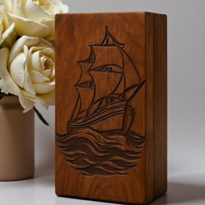 Solid wood engraved urn box with a symbolic sailing ship artwork, representing journey and serenity. Carefully crafted with secure bottom closure for safe ashes storage. Perfect for nautical-themed memorials, ocean lovers, and personalized remembrance.