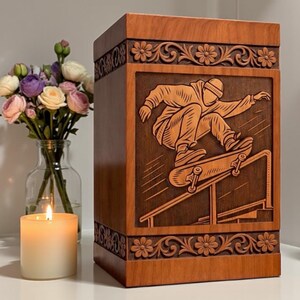 Personalized cremation urn box made from natural wood, featuring skateboard rider engraving, traditional floral borders, elegant finish, and memorial decor arrangement with candle.