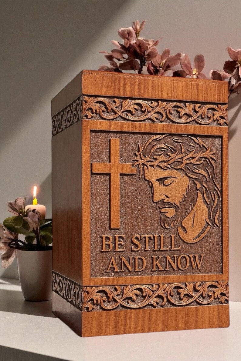 Close-up view of the “Be Still and Know” wooden cremation urn box showing intricate engraving of Jesus’ face and the cross. The fine detailing and smooth craftsmanship highlight premium wood texture and artisan engraving. A spiritual and meaningful Christian funeral urn representing comfort, belief, and everlasting memory.