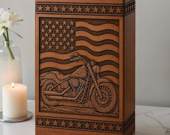 Könnte beinhalten: Eine rechteckige Urne aus Holz mit einem geschnitzten Relief eines Motorrads vor einer wehenden amerikanischen Flagge. Die oberen und unteren Ränder der Urne sind mit einer horizontalen Reihe geschnitzter Sterne in dunkelbrauner Holzoptik verziert.