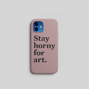 Pu&ograve; includere: Una custodia per telefono rosa polveroso con la scritta "Stay horny for art" in nero. La custodia del telefono ha un modulo fotocamera blu ed &egrave; posta su uno sfondo grigio chiaro.