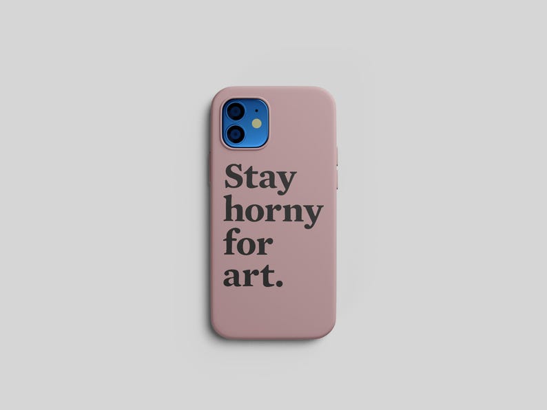 Pu&ograve; includere: Una custodia per telefono rosa polveroso con la scritta "Stay horny for art" in nero. La custodia del telefono ha un modulo fotocamera blu ed &egrave; posta su uno sfondo grigio chiaro.
