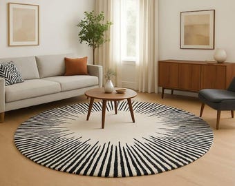 May include: A large circular area rug featuring a cream-colored center and a radiating pattern of black lines extending from the middle toward the outer edges. The rug is positioned on a light-colored wooden floor in a living room setting.