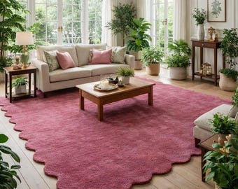 May include: A living room featuring a large, scalloped-edge, magenta rug. A beige sofa with pink and patterned pillows sits on the rug. The room is filled with potted plants, a wooden coffee table, and a side table with a lamp.