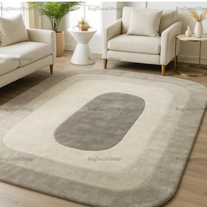 Könnte beinhalten: Ein rechteckiger Teppich mit einem geschichteten Design in Grau- und Cremetönen. Der Teppich hat eine zentrale ovale Form, die von konzentrischen Rechtecken umgeben ist und ein modernes, geometrisches Muster erzeugt. Der Teppich liegt auf einem Holzboden.