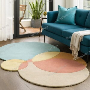 May include: A living room with two overlapping circular rugs in shades of blue, yellow, peach, and cream. A teal sofa with a matching cushion is visible. The rugs are a modern design.