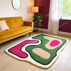 Könnte beinhalten: Moderner, abstrakter Teppich mit einzigartiger, organischer Form. Er hat einen cremefarbenen Rand, eine grüne Mittelfläche und pinkfarbene und beige Akzente. Eine schwarze Kontur definiert das Design.