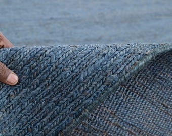 Puede incluir: Primer plano de una alfombra de yute trenzado azul. La textura de la alfombra es visible, con un patrón detallado de fibras tejidas. El borde de la alfombra está levantado, revelando la parte inferior. La alfombra es de color azul liso.