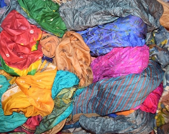 May include: A pile of colourful fabric remnants in shades of red, yellow, blue, green, and pink. The textiles appear to be silk or a similar lightweight material, with various patterns and textures. The image showcases a variety of fabrics.