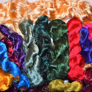 May include: A collection of colorful silk threads in various shades of green, blue, red, purple, and orange. The threads are arranged in a semi-circle, with the orange threads at the top.