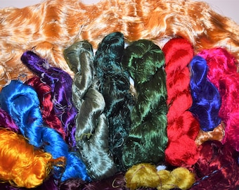 May include: A collection of colorful silk threads in various shades of green, blue, red, purple, and orange. The threads are arranged in a semi-circle, with the orange threads at the top.