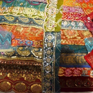 May include: A collection of colorful fabric strips with intricate embroidery, sequins, and beadwork. The fabrics feature a variety of colors, including teal, orange, red, and gold. The textiles appear to be of Indian or Middle Eastern origin.