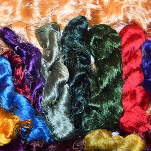 May include: A collection of colorful silk threads in various shades of green, blue, purple, red, and yellow. The threads are arranged in a pile, with some of the threads overlapping.