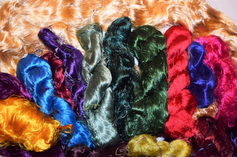 May include: A collection of colorful silk threads in various shades of green, blue, purple, red, and yellow. The threads are arranged in a pile, with some of the threads overlapping.