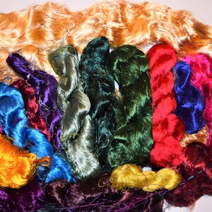 May include: A collection of colorful silk threads in various shades of green, blue, purple, red, and yellow. The threads are arranged in a semi-circle, with the ends of the threads overlapping.