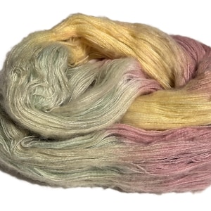 May include: A skein of hand-dyed yarn in a gradient of colors. The yarn transitions from pale green to yellow, then to pink. The fibers appear soft and fluffy, ideal for knitting or crocheting projects.