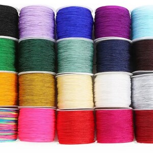 May include: Twenty spools of colorful waxed cord, each wound on a white plastic spool. The cords are in a variety of colors, including black, purple, blue, green, orange, gold, white, gray, red, pink, and multi-colored.