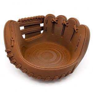 K&ouml;nnte beinhalten: Eine braune Sch&uuml;ssel in Form eines Baseballhandschuhs. Die Sch&uuml;ssel ist so gestaltet, dass sie einem Baseballhandschuh &auml;hnelt, mit detaillierten N&auml;hten und einer Tasche. Der Innenraum hat ein Holzmaserungsmuster. Der Handschuh hat eine hellbraune Farbe.