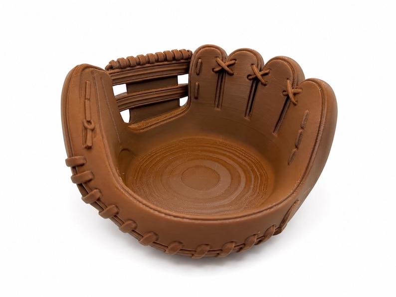K&ouml;nnte beinhalten: Eine braune Sch&uuml;ssel in Form eines Baseballhandschuhs. Die Sch&uuml;ssel ist so gestaltet, dass sie einem Baseballhandschuh &auml;hnelt, mit detaillierten N&auml;hten und einer Tasche. Der Innenraum hat ein Holzmaserungsmuster. Der Handschuh hat eine hellbraune Farbe.