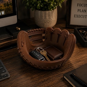 K&ouml;nnte beinhalten: Ein braunes, baseballhandschuhf&ouml;rmiges Tablett h&auml;lt Schl&uuml;ssel und eine Brieftasche. Das Tablett steht auf einem Holzschreibtisch, mit einem Computer, einer Tastatur und einem gerahmten Schild mit der Aufschrift "FOCUS PLAN EXECUTE".