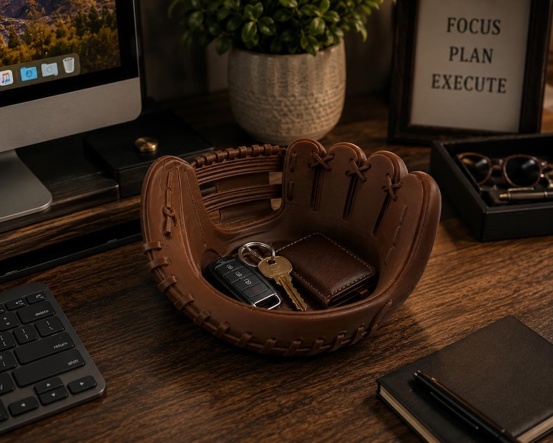 K&ouml;nnte beinhalten: Ein braunes, baseballhandschuhf&ouml;rmiges Tablett h&auml;lt Schl&uuml;ssel und eine Brieftasche. Das Tablett steht auf einem Holzschreibtisch, mit einem Computer, einer Tastatur und einem gerahmten Schild mit der Aufschrift "FOCUS PLAN EXECUTE".