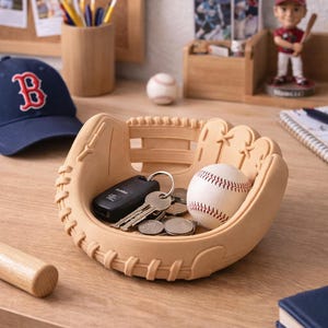 May include: A baseball glove-shaped desk organizer in a light tan color, holding keys, coins, and a baseball. A navy blue baseball cap with a red "B" logo is visible in the background. A baseball bat is also present.