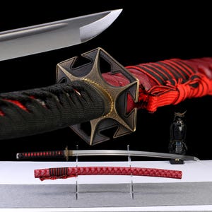 May include: A Japanese katana sword with a black handle and a red and black wrapped hilt. The blade is silver, and the scabbard is red. A small samurai figurine is also present.