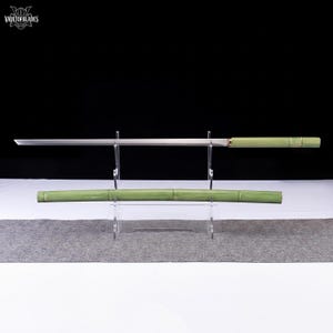 May include: A Japanese-style sword with a bamboo-style handle and scabbard. The blade is silver and straight, and the handle and scabbard are green. The sword is displayed on a clear stand against a black background.