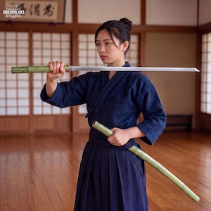 May include: A straight metal sword with a green bamboo-textured handle and matching scabbard. The blade is silver and polished, held horizontally. The scabbard is held in the other hand, angled downwards. The sword features a metallic collar.