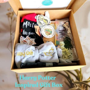 Può includere: Una confezione regalo a tema Harry Potter piena di vari oggetti. Include un calzino rosso e nero, un fiocco grigio con dettagli dorati, adesivi e una bacchetta. La scatola è marrone e presenta la scritta "Harry Potter Inspired Gift Box".