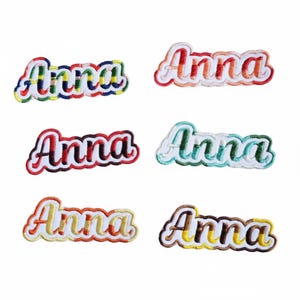 May include: Six embroidered patches with the name "Anna" in a cursive font. Each patch features a different colour scheme, including rainbow, red, teal, and brown. The patches have a white border.