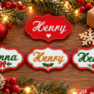 May include: Four embroidered name tags with scalloped edges. One red tag features the white name Henry with a heart. Three white tags feature the names Anna in green, Henry in gold, and Henry in green, each with festive holiday motifs.