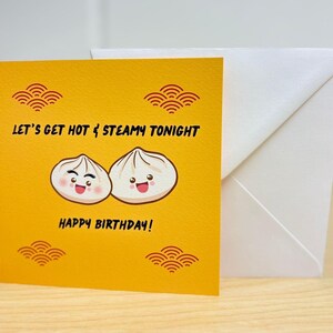 May include: A yellow birthday card with the text "LET'S GET HOT & STEAMY TONIGHT" and "HAPPY BIRTHDAY!" features two cartoon dumplings. A white envelope is behind the card. The card has decorative orange wave patterns.